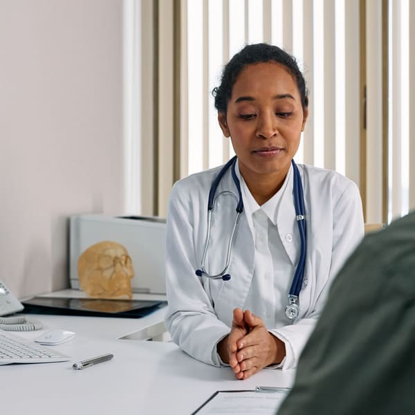 A pain medicine physician talks through treatment options with a patient across a desk at a clinic consultation.