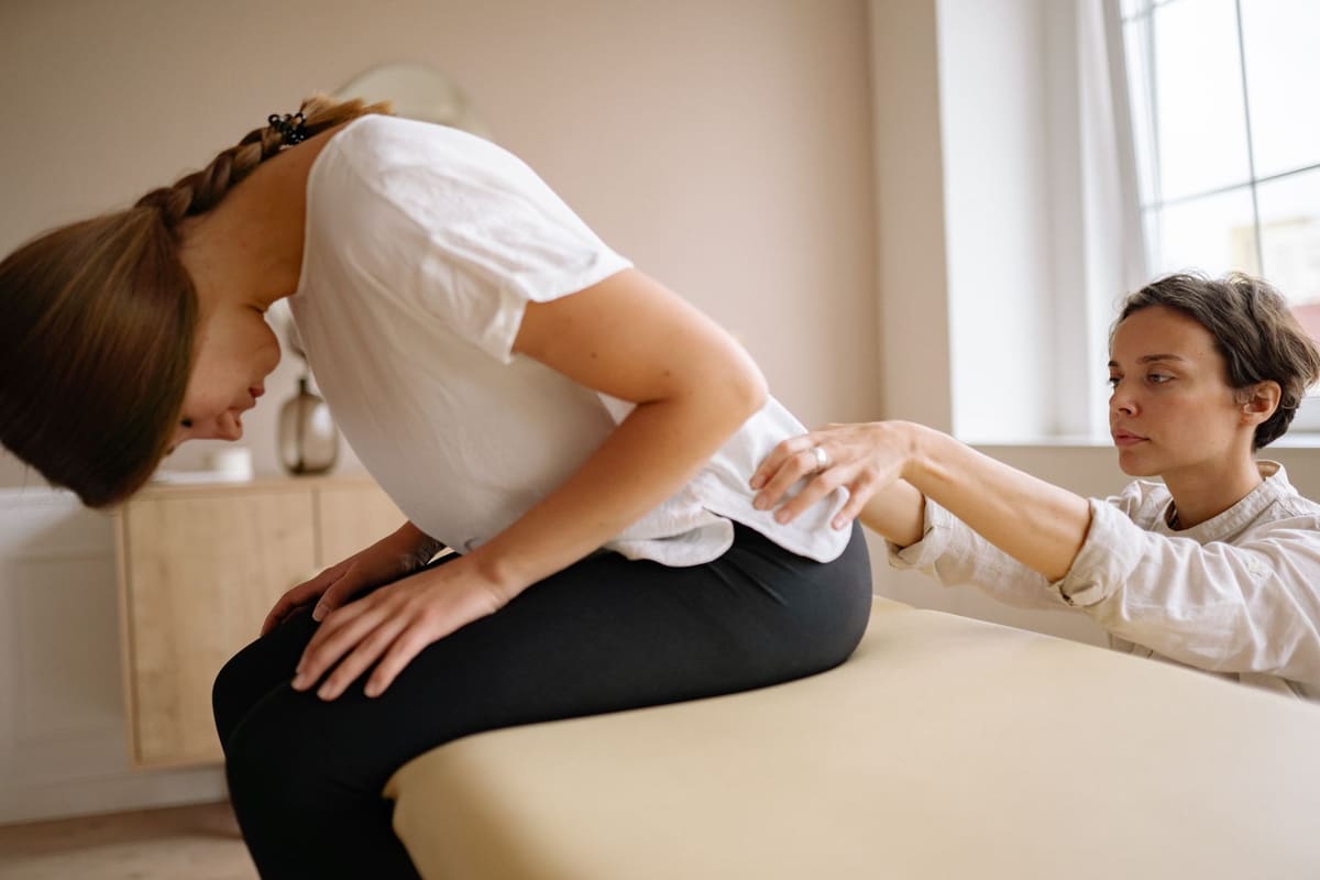 A physical therapist examines a seated patient's lower back during a treatment session at a pain clinic.